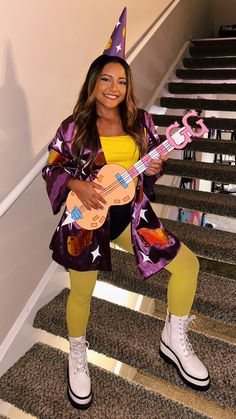 a woman is holding a guitar and wearing a party hat while standing on some stairs