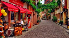 a cobblestone street lined with shops and stores on both sides, surrounded by greenery