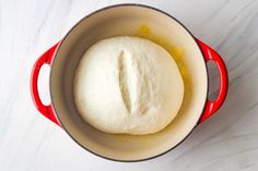 a ball of bread in a red pot on a white counter top with yellow liquid