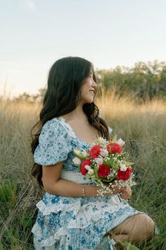 a woman sitting in the grass holding a bouquet of flowers