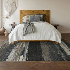 a bed with white sheets and pillows on top of a wooden floor next to a window