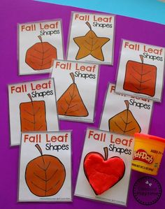 four fall leaf shapes are displayed on a purple surface with an orange cup and two red apples