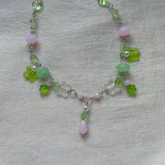 a green and pink beaded necklace on a white cloth with beads in the shape of flowers