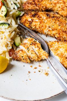 a white plate topped with chicken, pasta and vegetables next to a fork and knife