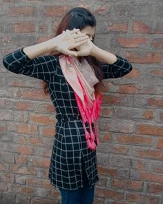 a woman standing in front of a brick wall covering her eyes