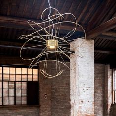 an artistic light hanging from the ceiling in a room with brick walls and exposed ceilings