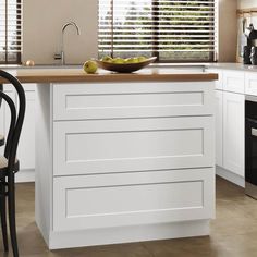 a bowl of fruit is on the counter top in this modern kitchen with white cabinets and black chairs