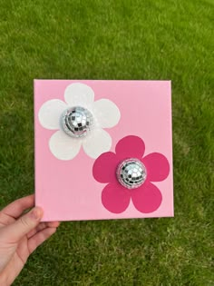 a hand holding up a pink and white flower with two silver knobs on it