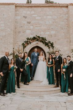 a group of people standing in front of a stone building with flowers and greenery