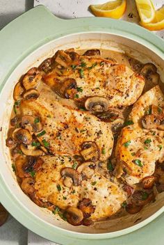 chicken with mushrooms and lemons in a white dish on a table next to sliced oranges