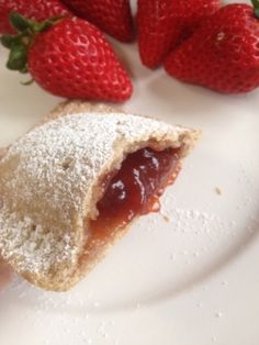 some strawberries are sitting on a plate next to a piece of food that is covered in powdered sugar