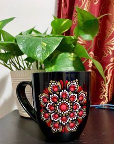 a black coffee mug sitting on top of a table next to a potted plant