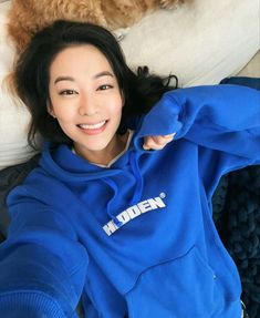 a woman in a blue hoodie laying down next to a dog on a couch