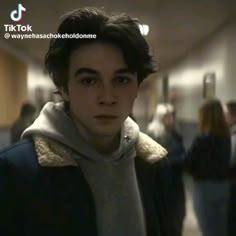 the young man is wearing a scarf around his neck and looking at the camera while standing in an office hallway