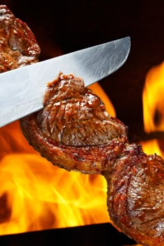 a steak being cooked on a grill with flames in the background and a large knife sticking out of it