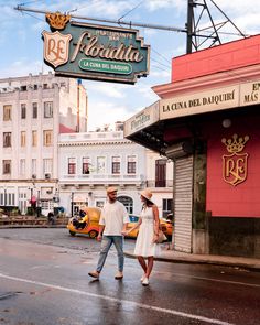 a man and woman walking down the street in front of a building with a sign above it