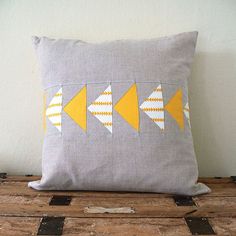 a gray pillow with yellow arrows on it sitting on a wooden table next to a white wall