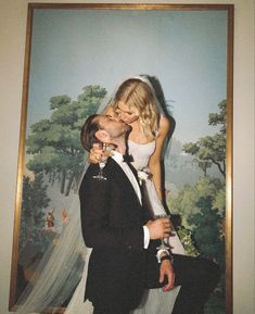 a bride and groom kissing in front of a painting