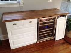 an open wine cooler in the middle of a kitchen with wood floors and white cabinets