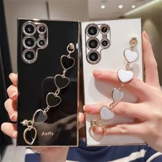 a woman holding up two cell phones with heart charms in their cases, one is white and the other is gold