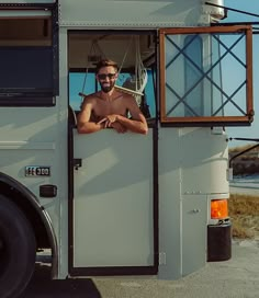 a shirtless man standing in the doorway of a white bus looking at the camera