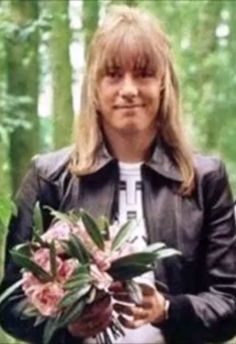 a woman holding flowers in her hands and wearing a leather jacket with trees in the background