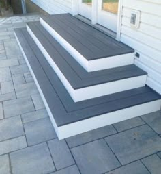 three steps leading up to the front door of a white house with black and gray trim