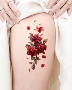 a woman's thigh with red roses on it and her hands behind her back