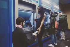 people standing in line to get their tickets at an atm machine while another man looks on