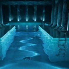 an indoor swimming pool in the middle of a building with columns and lights on either side