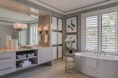 a large white bath tub sitting next to a bathroom window covered in shuttered blinds