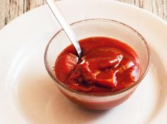 a spoon in a small glass bowl filled with ketchup on top of a white plate