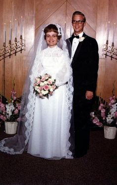 a man and woman standing next to each other in front of a wall with candles