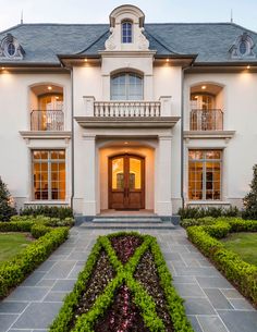 a large white house with lots of windows and plants in the front garden area at dusk