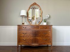 a dresser with a mirror and lamp on top of it in front of a wall