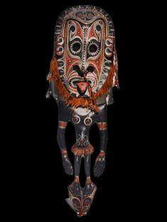 an african mask hanging from the ceiling in front of a black background with red and orange accents