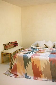 a bed sitting in a bedroom next to a wooden table and chair with pillows on it