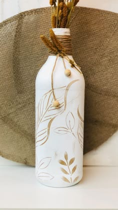 a white vase with dried flowers in it sitting next to a burlap hat