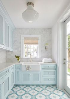 a blue and white kitchen with tile flooring, cabinets, sink and window in the corner