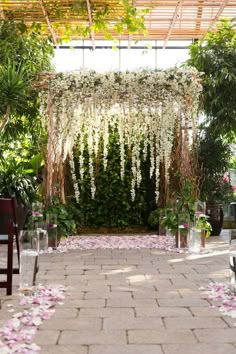 an outdoor wedding venue with flowers and greenery on the aisle, in front of a pergolated area