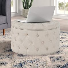 a laptop sitting on top of a round ottoman in a living room with blue carpet