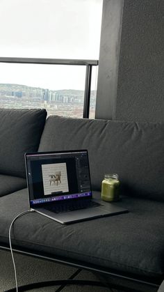 an open laptop computer sitting on top of a gray couch next to a canister