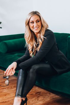 a woman sitting on top of a green couch wearing black pants and high heeled shoes