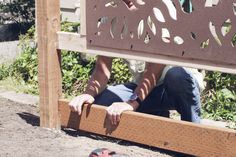 a man sitting on the ground next to a wooden bench with holes cut in it