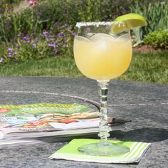 a margarita sitting on top of a table next to a magazine and drink glass with a lime wedge in it