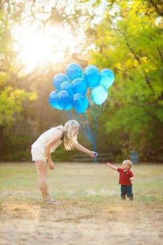 a woman and child flying blue balloons in a field with the sun shining down on them