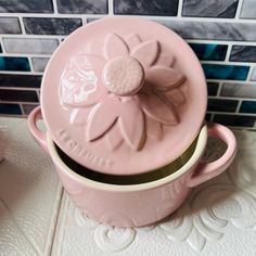 a pink ceramic pot with a flower on the lid sitting on a tile counter top