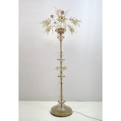 a glass and metal lamp with flowers on the top is sitting on a white surface