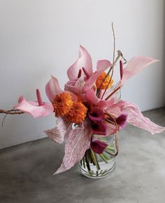 a vase filled with pink and orange flowers sitting on top of a cement floor next to a white wall