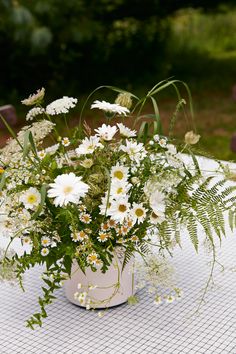 a vase filled with lots of white flowers on top of a table covered in greenery